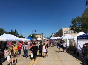 Outdoor craft vendor fair with people walking among tents and booths lined on street