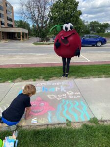 Cranberry Guy standing on side of street + kid drawing with chalk on sidewalk