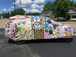 Car covered in handmade quilt and parked in driveway